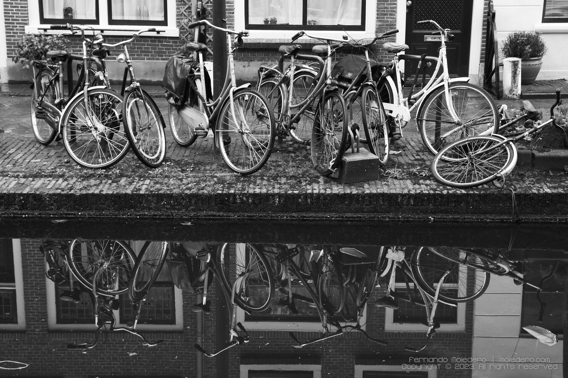Row of bicycles parked along a canal with reflections in the water, black and white street photography in Delft, the Netherlands