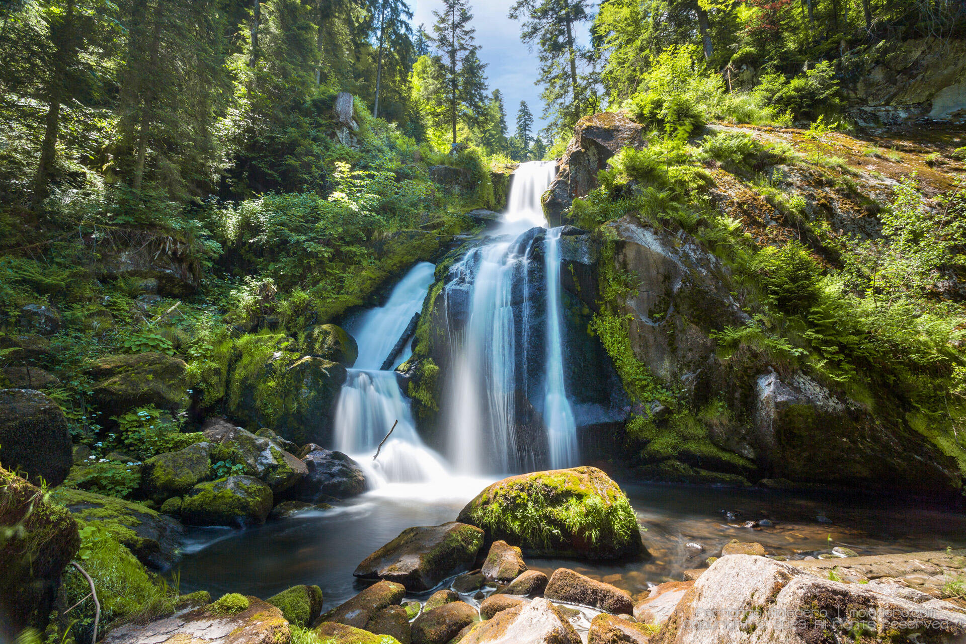 Long-exposure photo of Triberg Waterfalls in the Black Forest, Baden-Württemberg, Germany, with water flowing down mossy rocks surrounded by dense green forest