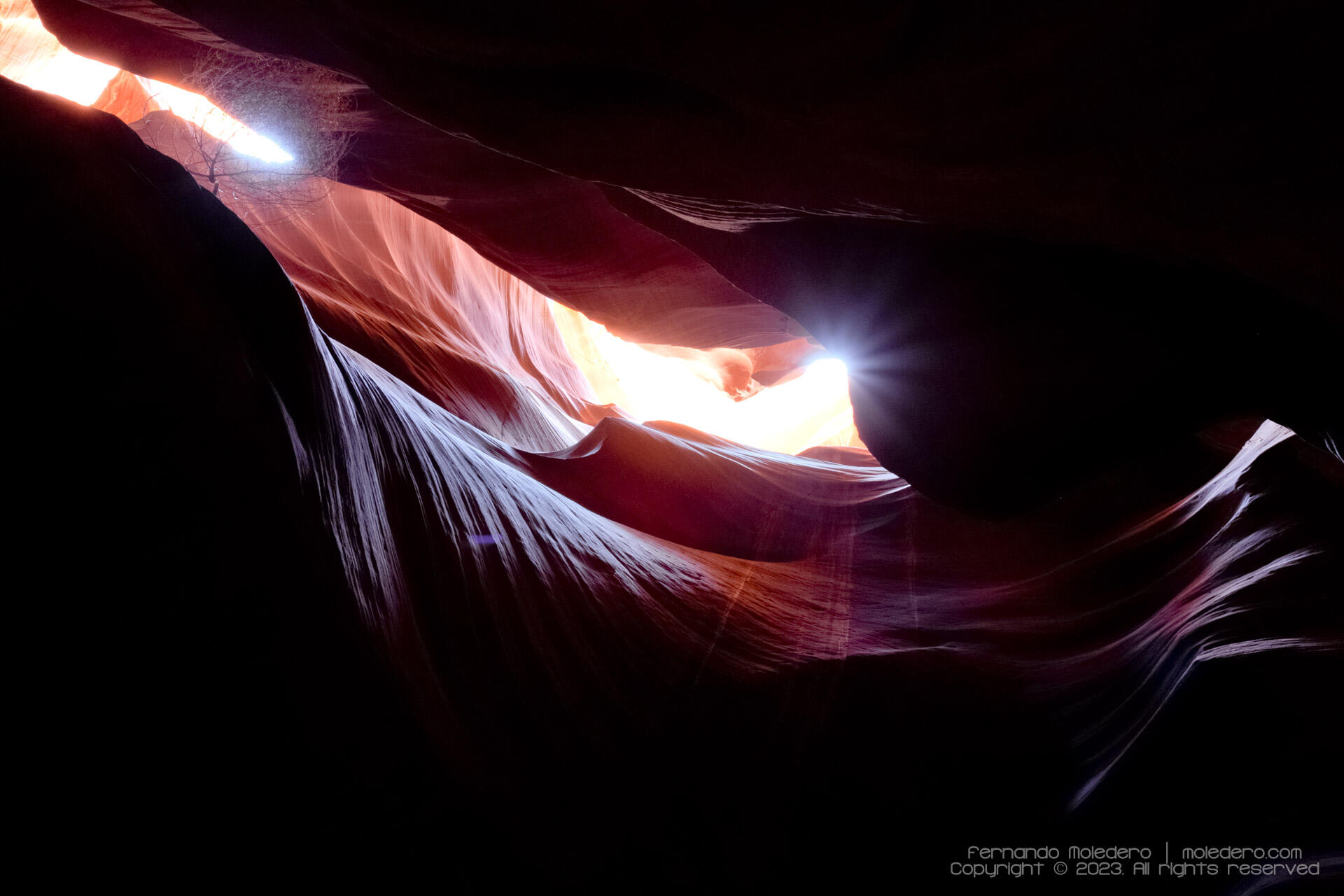 View from the depths of Antelope Canyon, Arizona, USA, showing sunlight entering from above and illuminating the curved sandstone walls with dramatic contrasts of light and shadow
