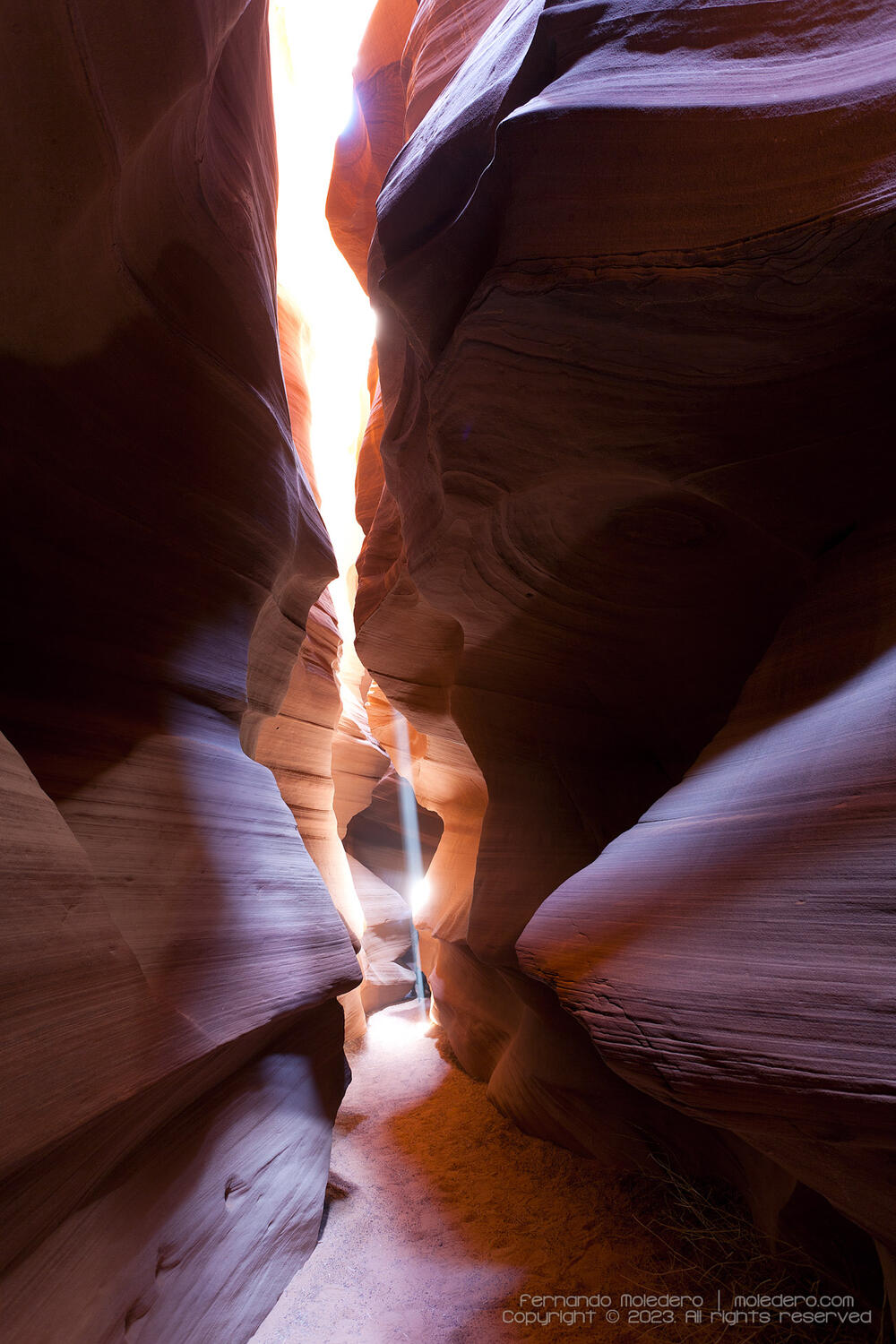 View inside Antelope Canyon, Arizona, USA, showing a narrow sandstone corridor with soft sunlight filtering down, illuminating the curved red rock walls and sandy floor