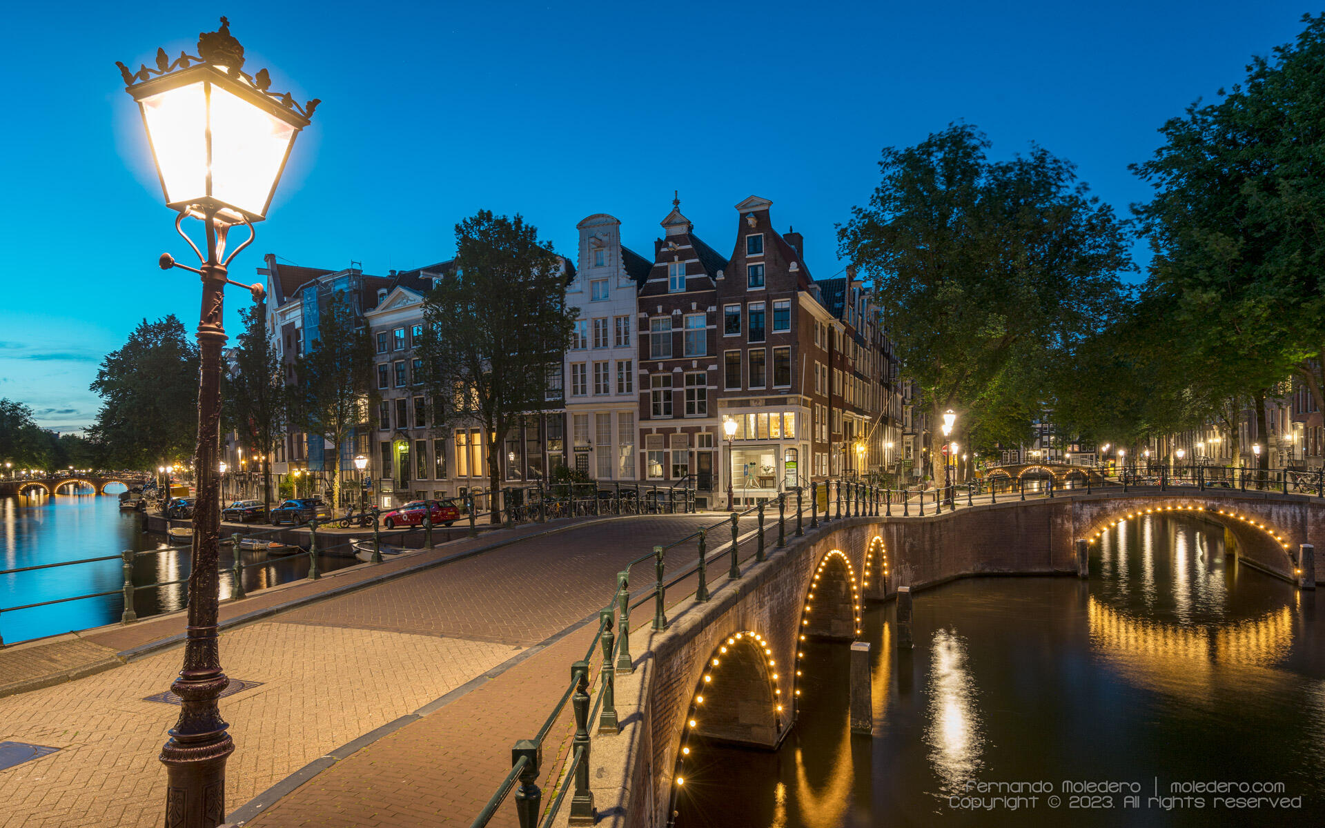 Evening view of the Keizersgracht and Leidsegracht canals crossing in Amsterdam, Netherlands, with illuminated arched bridges, historic canal houses and reflections on the water