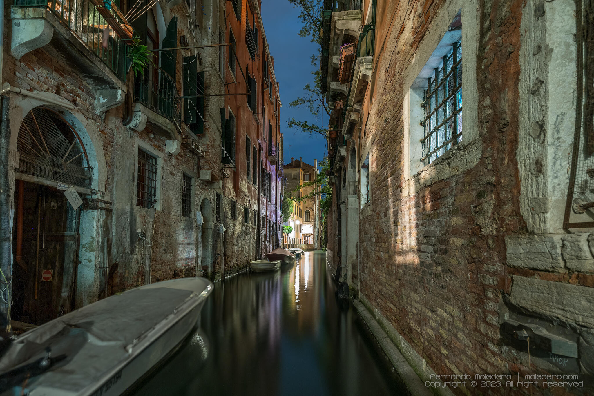 Peaceful night scene of a narrow canal in Venice, Italy, with old brick buildings, small boats and soft light reflecting on the water