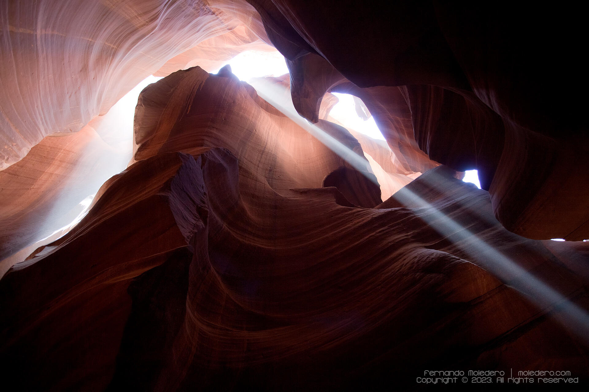 Sunlight streaming through narrow sandstone walls of Antelope Canyon in Arizona, creating dramatic light beams and shadows