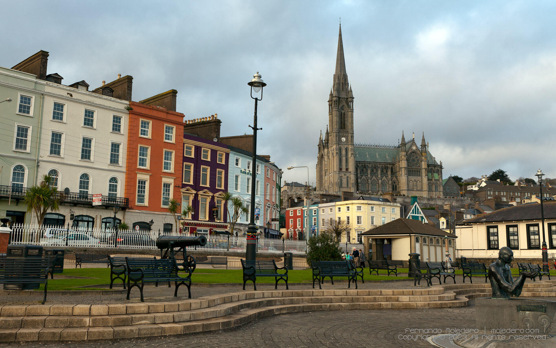 View of the colorful houses along Cobh waterfront in County Cork, Ireland, with the tall spire of St. Colman’s Cathedral dominating the skyline