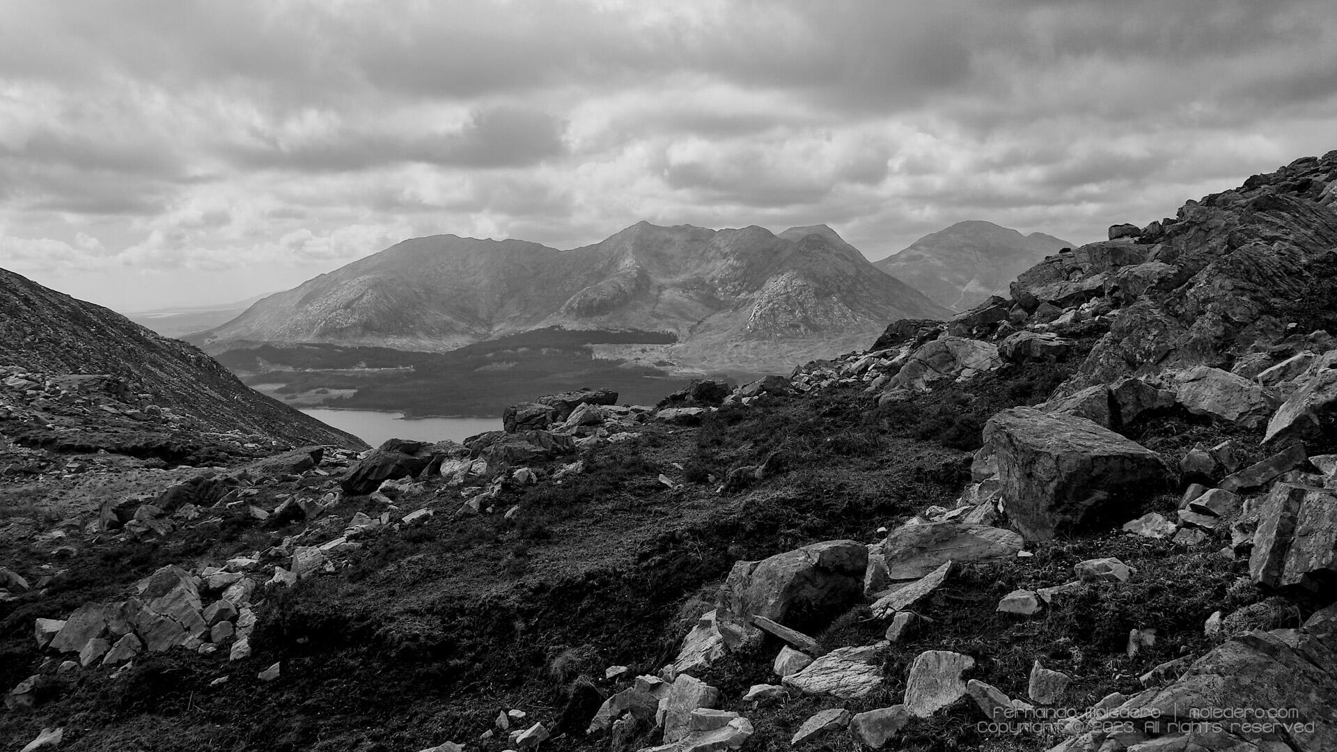 Black and white photograph of the Maumturks mountains in Connemara, Ireland, with rocky foreground and dramatic clouds above