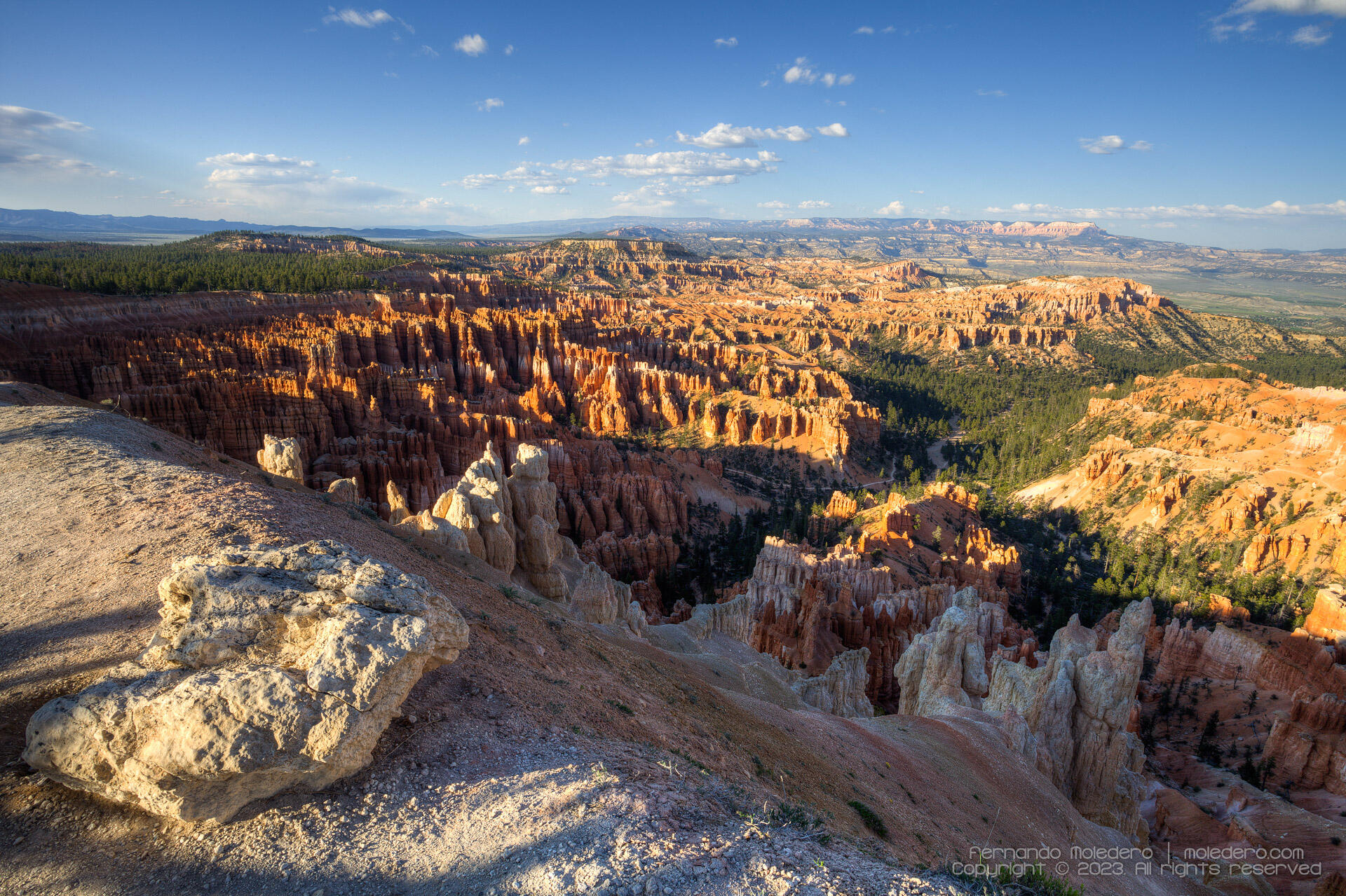 Wide-angle landscape of Bryce Canyon National Park in Utah, USA, showing the natural amphitheater of orange and red hoodoos, pine forests, and distant plateaus under a clear blue sky