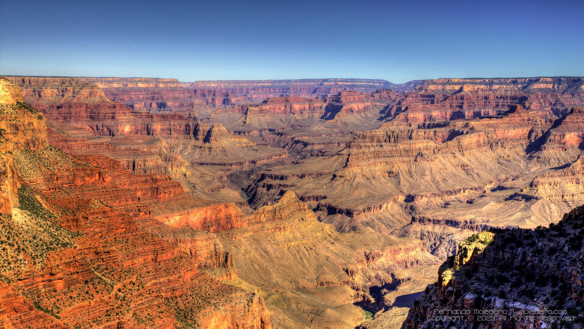 Panoramic landscape of the Grand Canyon in Arizona, USA, showing vast layered cliffs, colorful rock formations and deep valleys under a clear blue sky