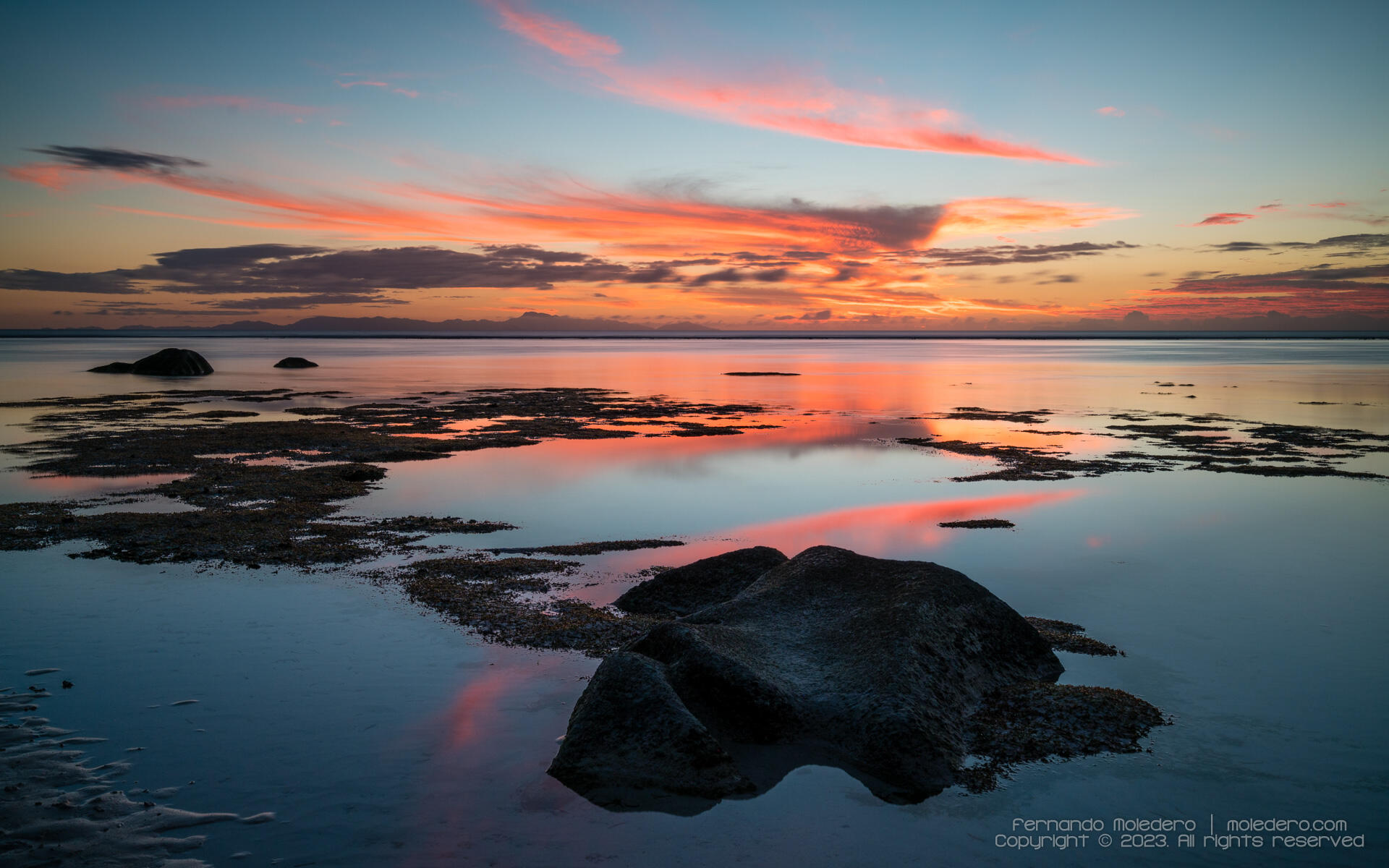 Colorful sunset over Anse Source d’Argent beach on La Digue Island, Seychelles, with calm ocean water, scattered rocks and reflections of orange and pink clouds in the lagoon