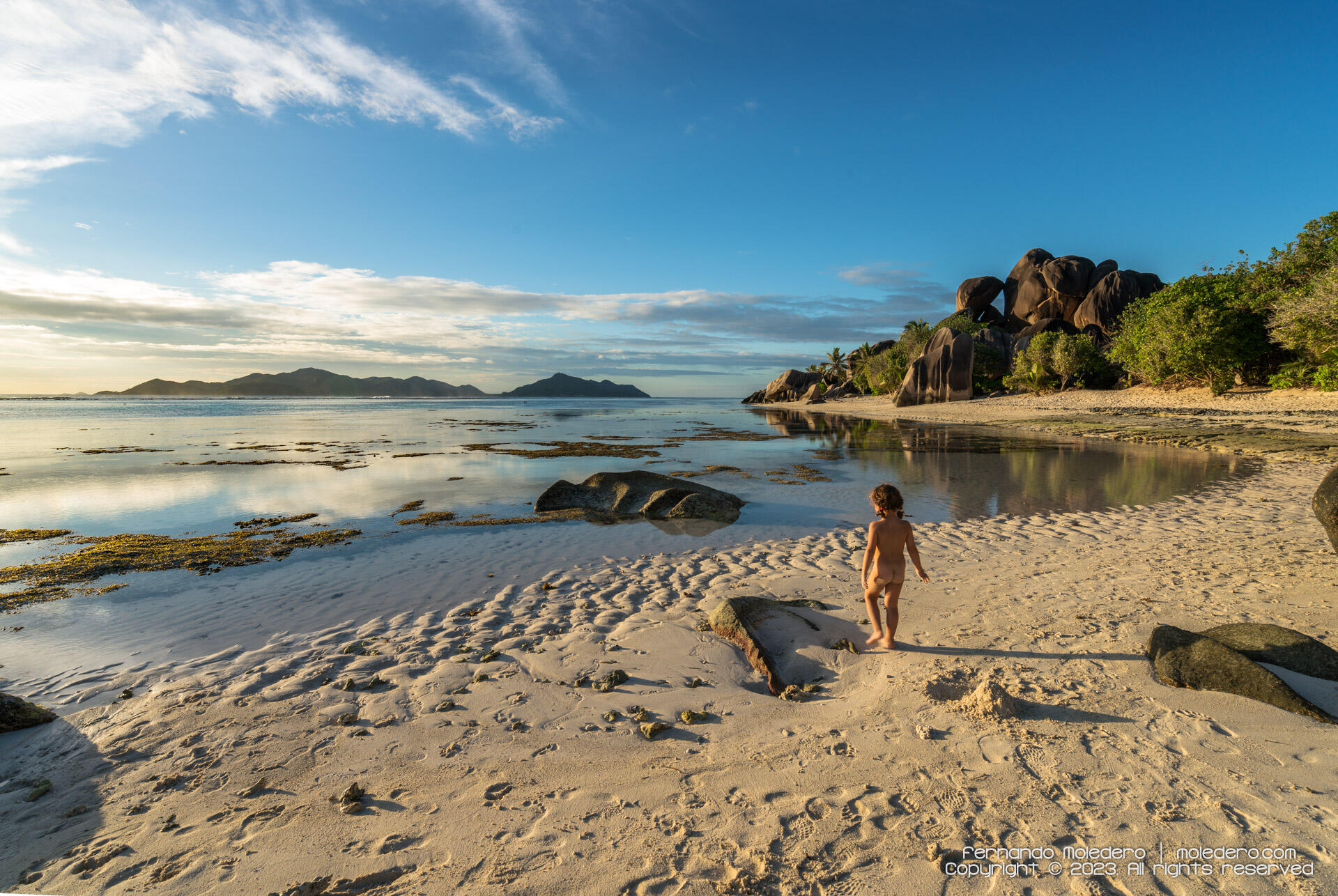 Panoramic view of Anse Source d'Argent beach on La Digue island, Seychelles, showing granite boulders, white sand and calm sea under a clear sky at sunset