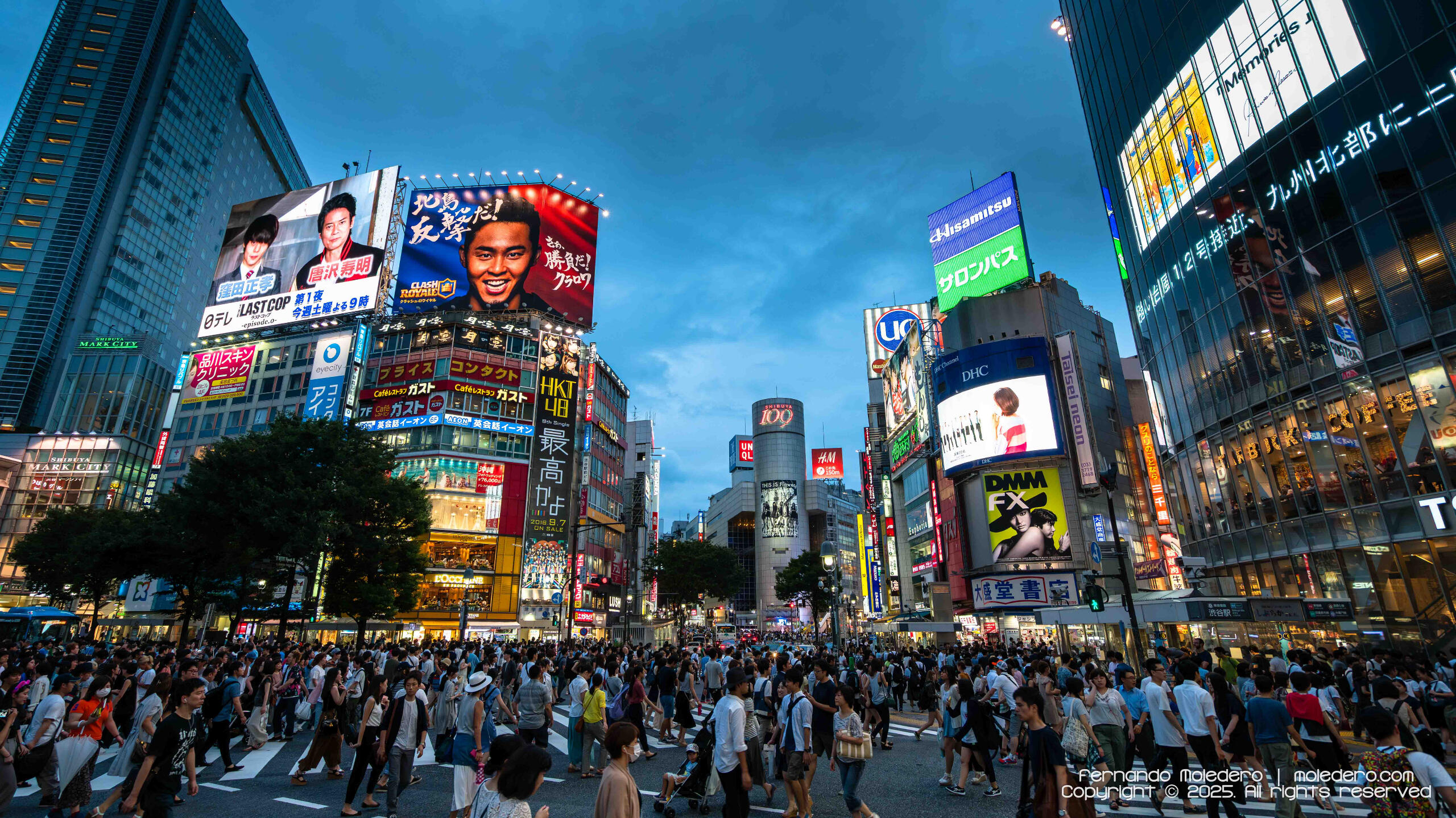 Crowds of people crossing Shibuya Crossing in Tokyo, Japan, surrounded by illuminated billboards and buildings at dusk