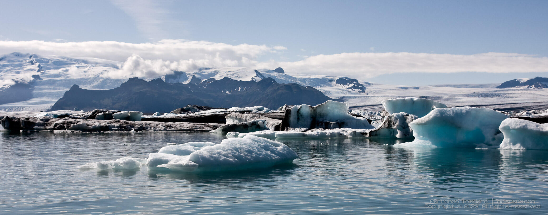 Panoramic view of Jökulsárlón Glacier Lagoon in Iceland, showing icebergs drifting in turquoise waters with Vatnajökull glacier and mountains behind