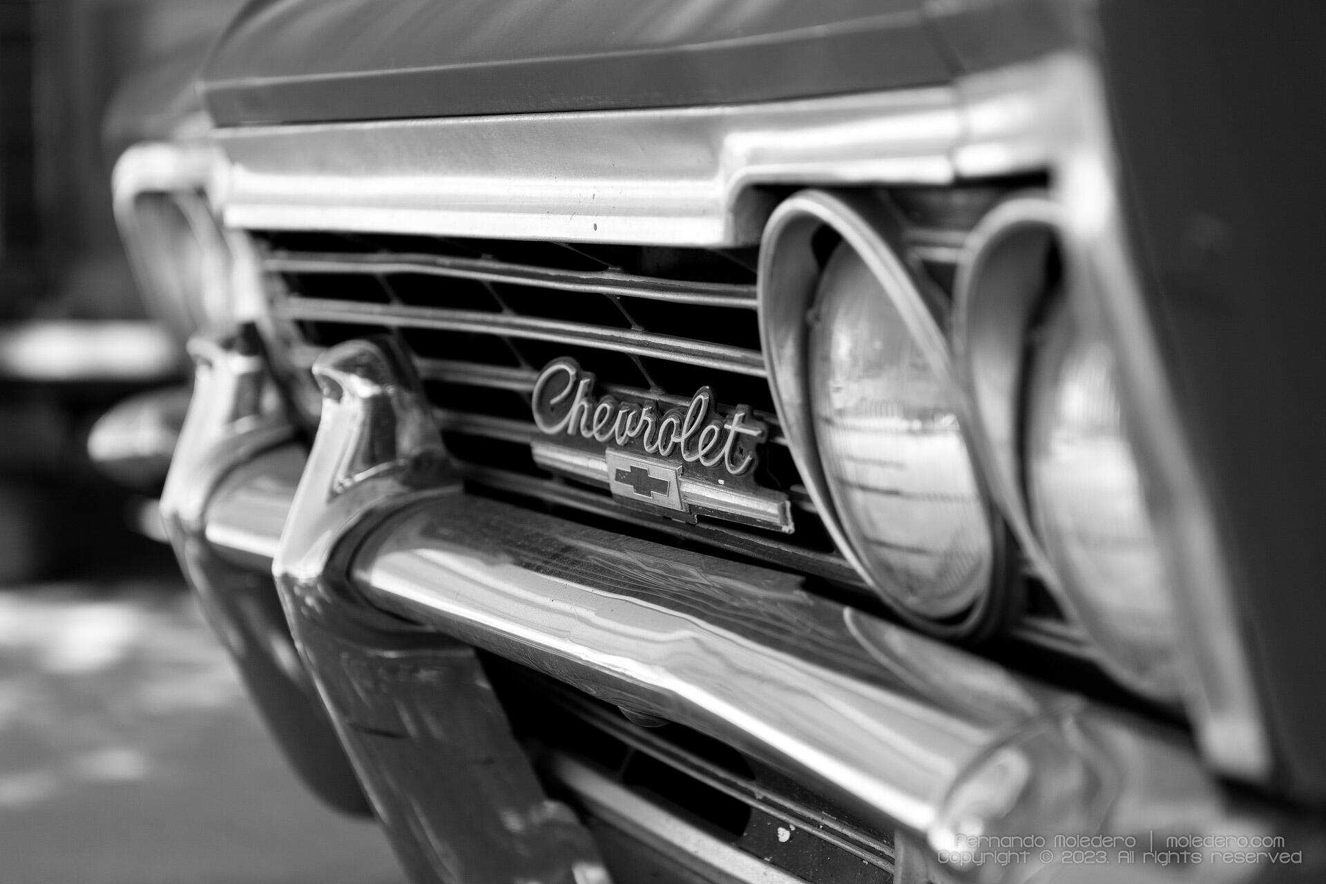 Close-up black and white photo of the front grille and headlights of a 1967 Chevrolet Impala, showing the Chevrolet emblem and chrome details
