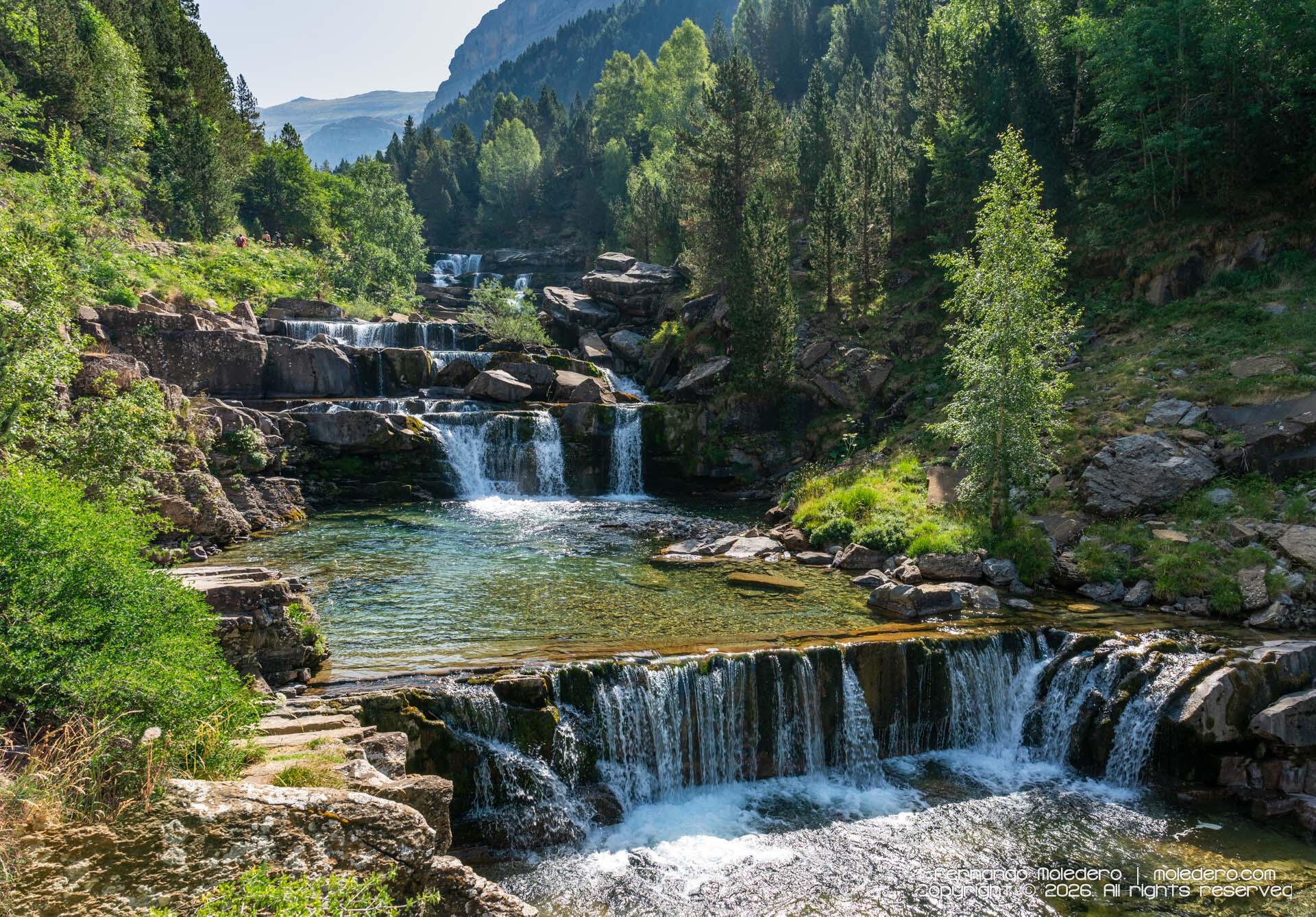 A succession of mountain waterfalls descends through the Gradas de Soaso, carving its way along the crystal-clear Arazas River in Ordesa y Monte Perdido National Park. The cascading water creates a natural staircase through one of the most spectacular land