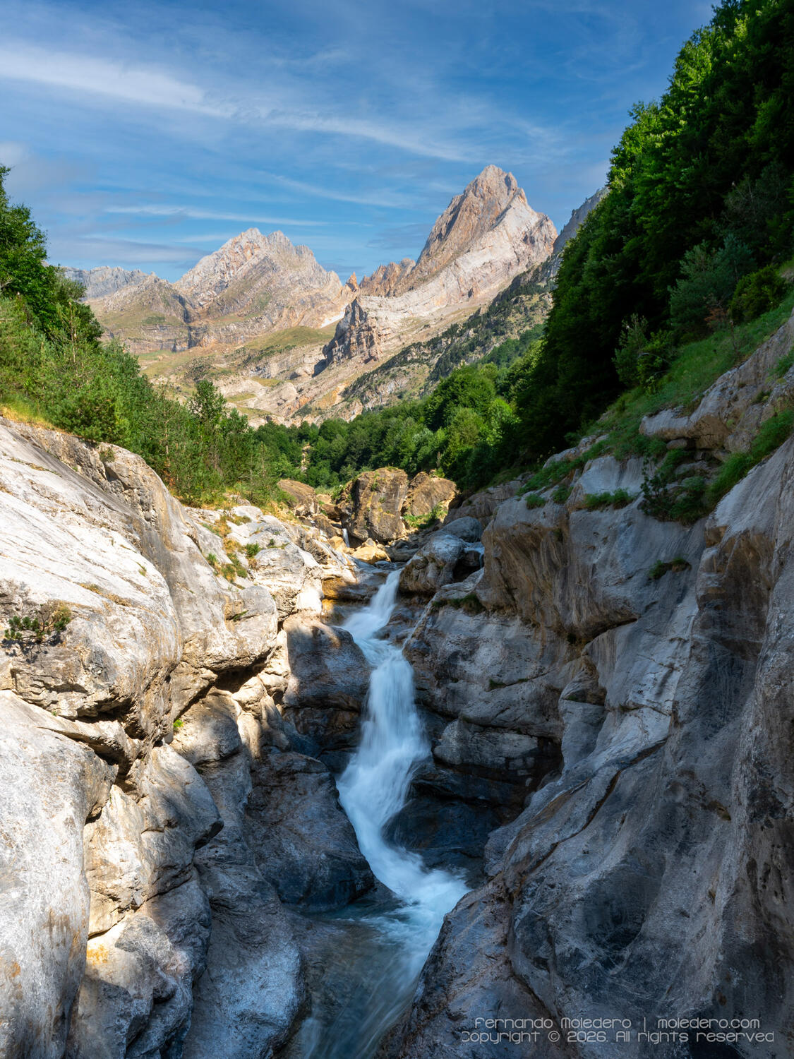 Long-exposure landscape photograph of one of the Cascadas de La Larri in the Pineta Valley, Huesca, Spain, with rushing mountain water flowing through a rocky gorge beneath the dramatic limestone peaks of the Spanish Pyrenees
